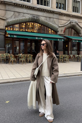 a lady in a white sweater, a pair of white pants and a brown long cashmere wool coat